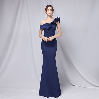 Frau in elegantem, schulterfreiem, dunkelblauem Abendkleid mit Rüschen, posiert vor grauem Hintergrund. Elegante Mode, Abendgarderobe, Damenkleidung.