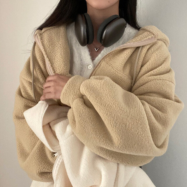 Frau in beiger Teddyjacke mit Kopfhörern um den Hals, hält weiße Decke. Modetrend, Herbstmode, gemütlicher Look, Damenbekleidung.