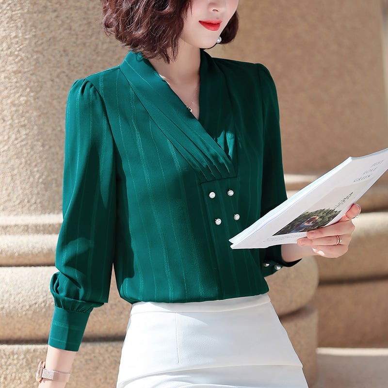 Frau in eleganter, grüner Bluse mit V-Ausschnitt und Perlenknöpfen, hält ein Buch. Stilvolle Mode, Business-Look, Damenbekleidung.