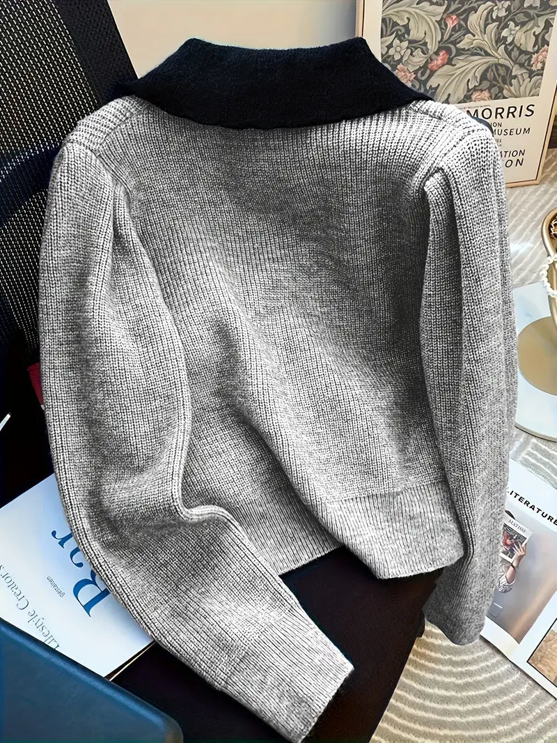 Grauer Strickpullover mit schwarzem Kragen auf einem Stuhl, umgeben von Büchern und Zeitschriften. Elegante Herbstmode, gemütlicher Stil.