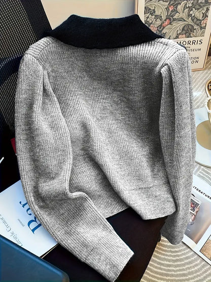 Grauer Strickpullover mit schwarzem Kragen auf einem Stuhl, umgeben von Büchern und Zeitschriften. Elegante Herbstmode, gemütlicher Stil.