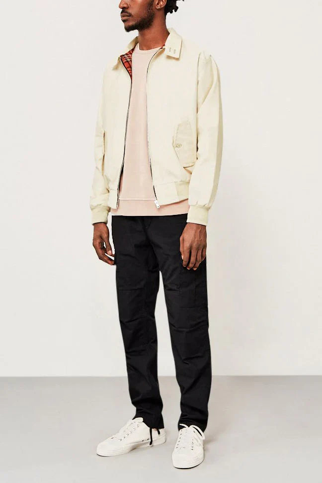 Mann in beiger Harrington-Jacke, schwarzer Hose und weißen Sneakers vor weißem Hintergrund. Modischer Freizeitlook für Herren.