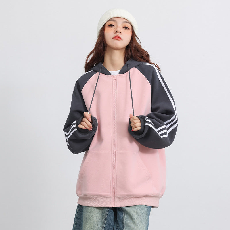 Frau in rosa Kapuzenpullover mit grauen Ärmeln und Streifen, trägt weiße Mütze und Jeans. Modetrend, lässiger Stil, Streetwear.