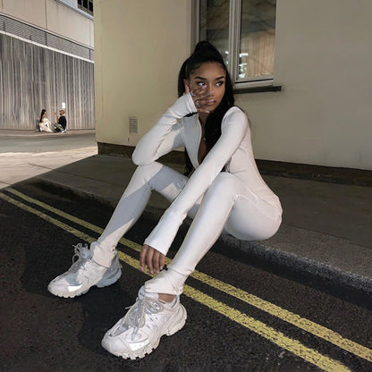 Frau in weißem Outfit und Sneakern sitzt auf Bordstein, Nachtaufnahme, urbaner Hintergrund. Streetwear, Mode, Nachtfotografie, stilvoll.