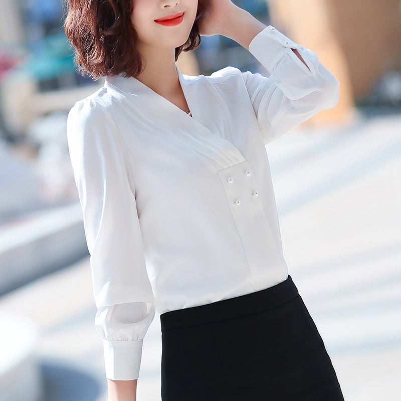 Frau in eleganter weißer Bluse mit V-Ausschnitt und Perlendetails, kombiniert mit schwarzem Rock. Businessmode, stilvoll, modern.