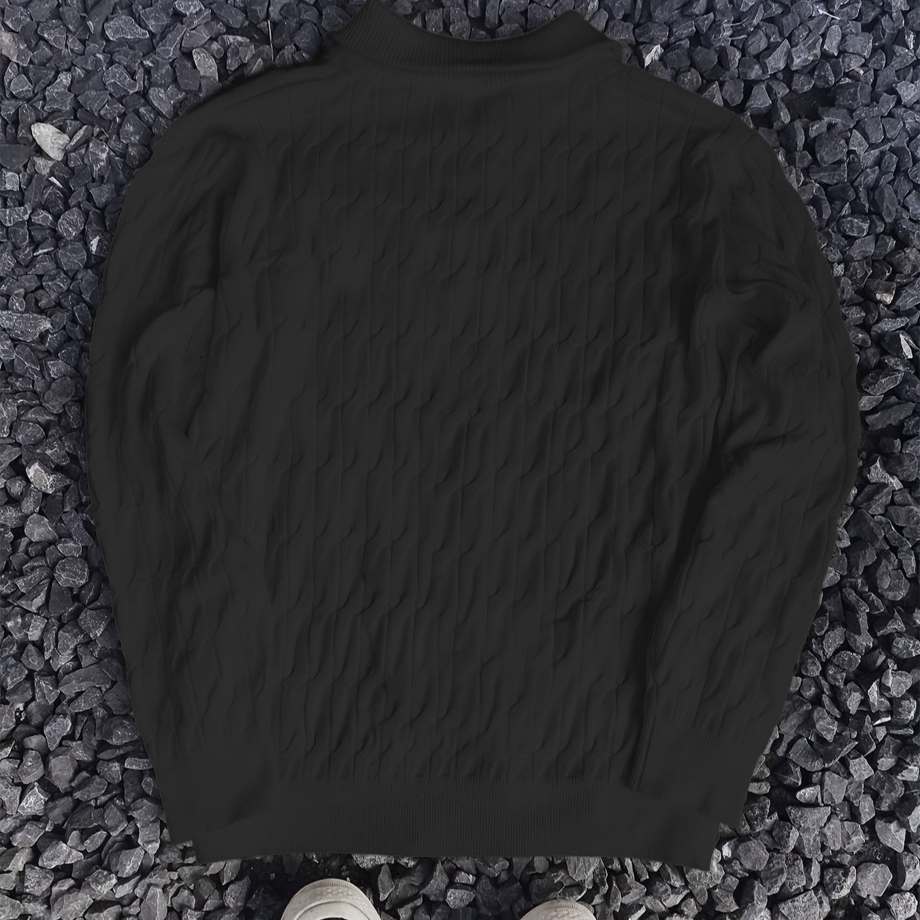 Schwarzer Strickpullover mit Zopfmuster auf grauem Kieshintergrund, modisch und elegant, ideal für Herbst- und Wintermode.