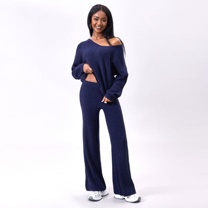 Frau in dunkelblauem Strick-Zweiteiler mit weitem Pullover und Hose, lächelt, trägt weiße Sneaker, modisches Freizeitoutfit, Studioaufnahme.