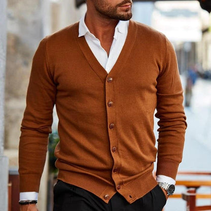 Mann in braunem Cardigan und weißem Hemd, stilvoll gekleidet, geht auf einer städtischen Straße. Elegante Herrenmode, Herbstoutfit, urbane Mode.