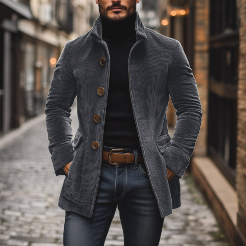 Mann in grauem Cordmantel und schwarzem Rollkragenpullover auf Kopfsteinpflasterstraße. Modischer Herbstlook, urbane Herrenmode, stilvolle Jacke.