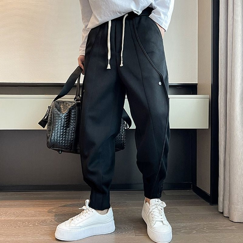 Mann in schwarzer Jogginghose mit weißen Schnürsenkeln und weißen Sneakers, hält eine schwarze Tasche. Moderne Herrenmode, lässiger Stil.