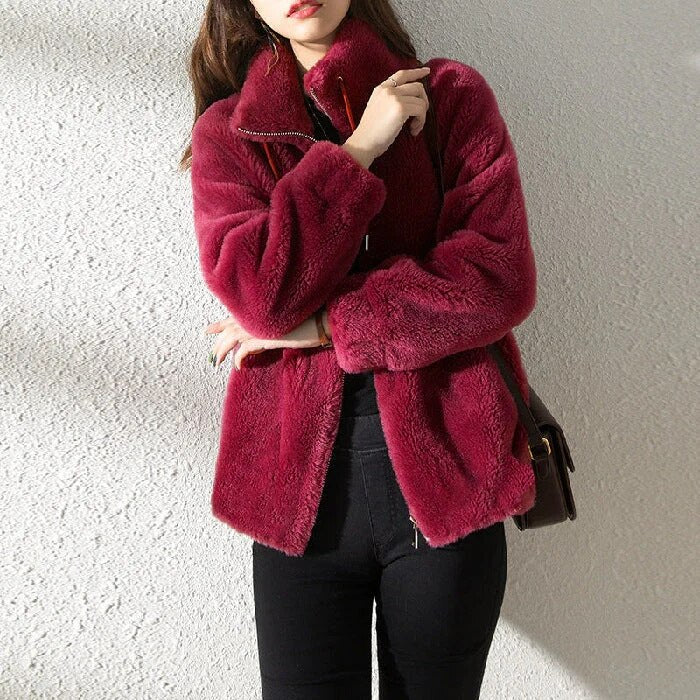 Frau in roter Kunstpelzjacke, schwarze Hose, vor weißer Wand. Modetrend, Wintermode, stilvolle Damenbekleidung, warme Jacke.