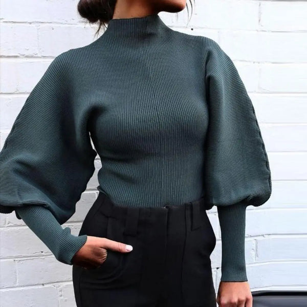 Dunkelgrüner Pullover mit Ballonärmeln, kombiniert mit schwarzer Hose vor weißer Ziegelwand. Modetrend, eleganter Damenstil, Herbstmode.