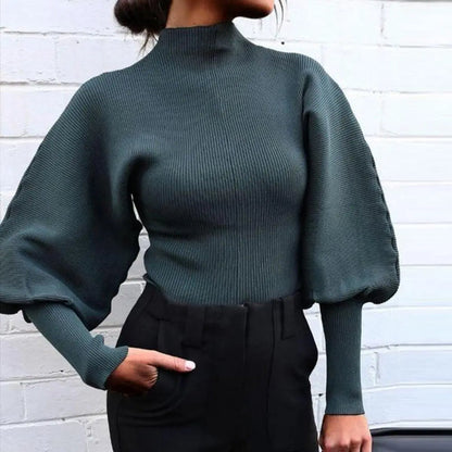Dunkelgrüner Pullover mit Ballonärmeln, kombiniert mit schwarzer Hose vor weißer Ziegelwand. Modetrend, eleganter Damenstil, Herbstmode.