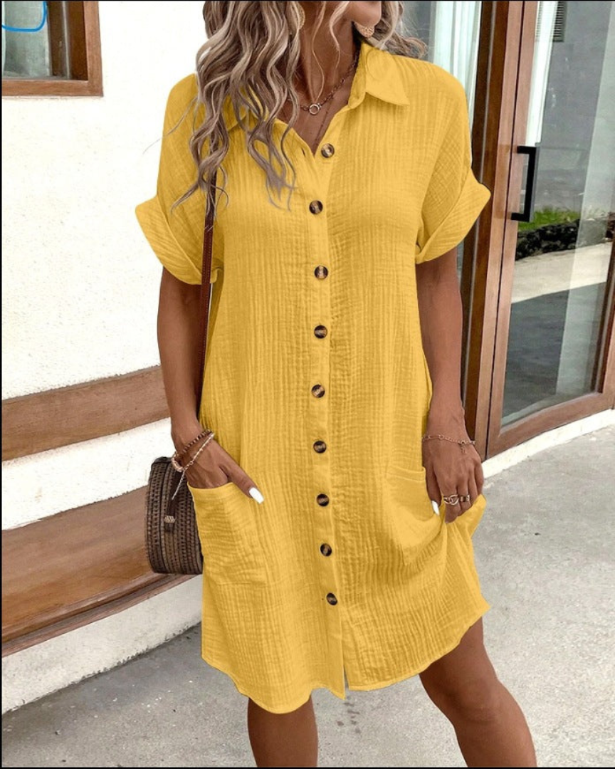 Frau in gelbem Hemdkleid mit Knopfleiste, lässig und sommerlich, steht vor modernem Gebäude. Perfekt für Sommermode und Freizeitkleidung.