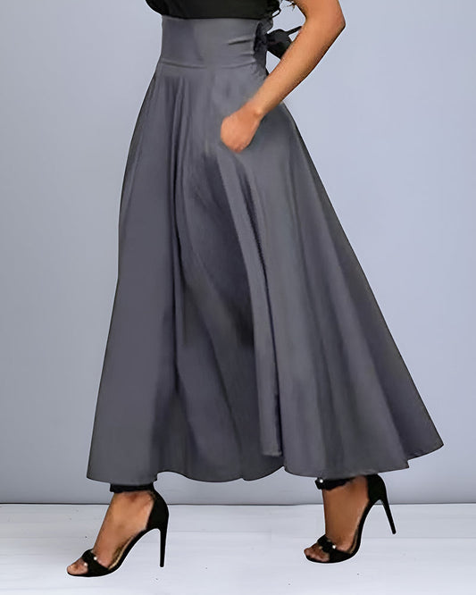 Damen grauer Maxirock mit hoher Taille, fließendem Stoff und Seitentaschen, kombiniert mit schwarzen High Heels. Elegante Mode für besondere Anlässe.