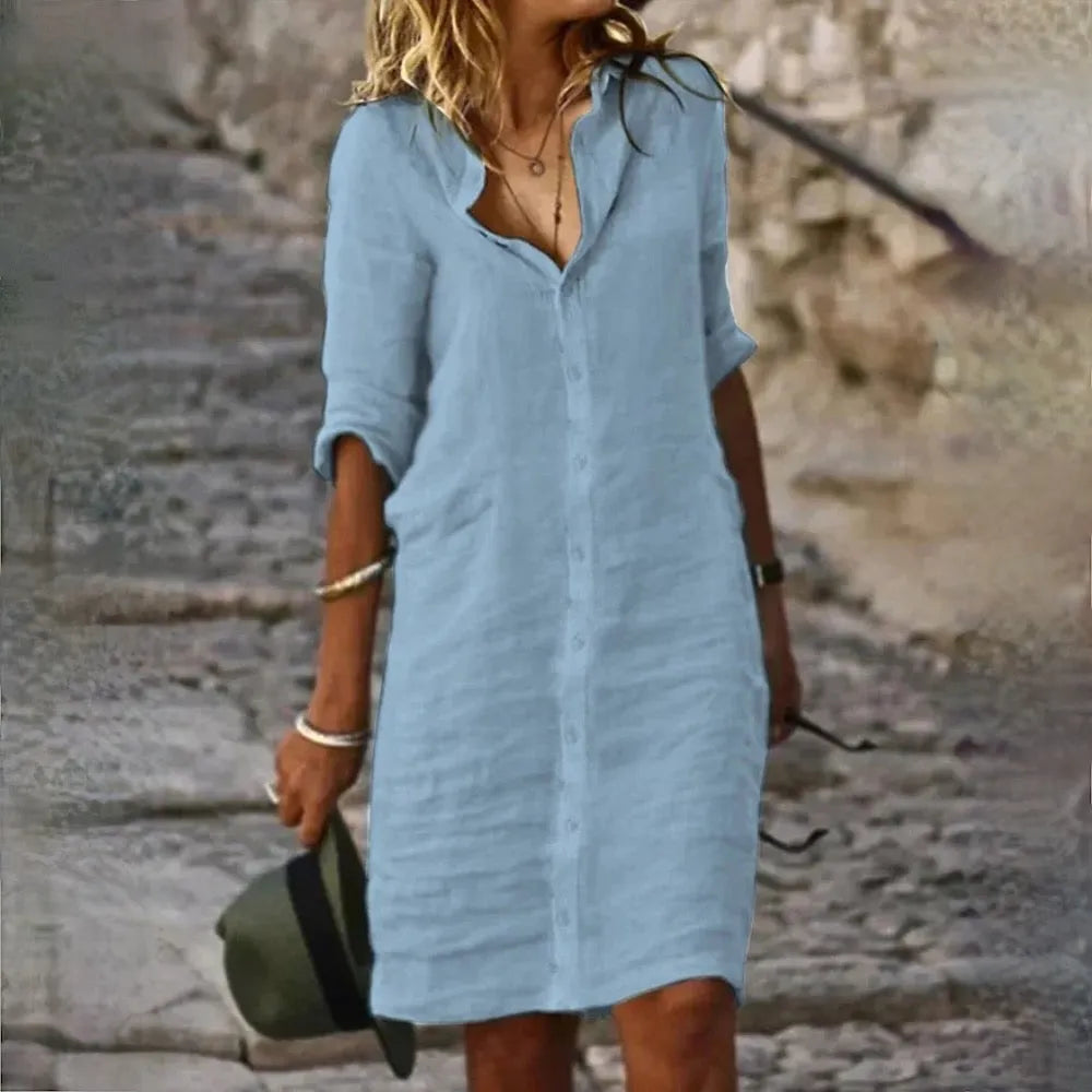 Frau in hellblauem Leinenkleid auf steiniger Treppe, hält Hut in der Hand. Sommermode, lässiger Stil, Outdoor, Freizeitkleidung.