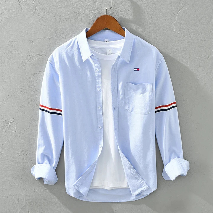 Hellblaues Herrenhemd mit Brusttasche und gestreiften Ärmeln, auf Holzkleiderbügel. Modisches Freizeitkleidungsstück für Männer.