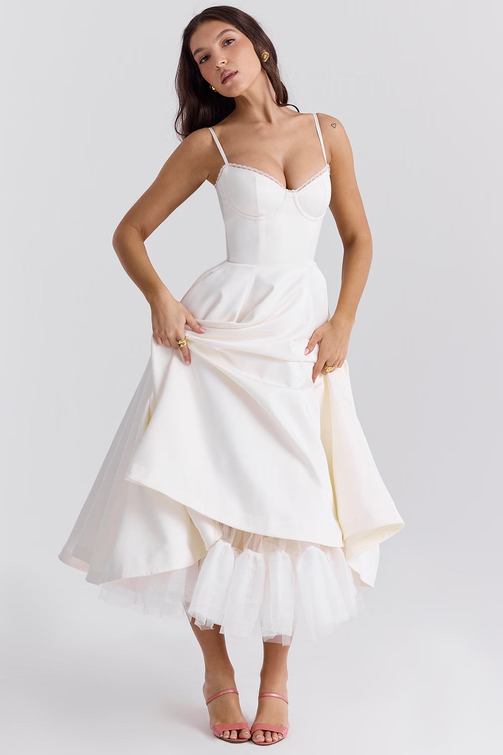 Frau in elegantem, weißem Cocktailkleid mit Spaghettiträgern und ausgestelltem Rock, posiert vor neutralem Hintergrund. Perfekt für Abendmode und Hochzeiten.