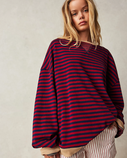 Junge Frau in übergroßem, gestreiftem Pullover in Rot und Blau, kombiniert mit gestreifter Hose. Modetrend, lässiger Stil, Herbstmode.