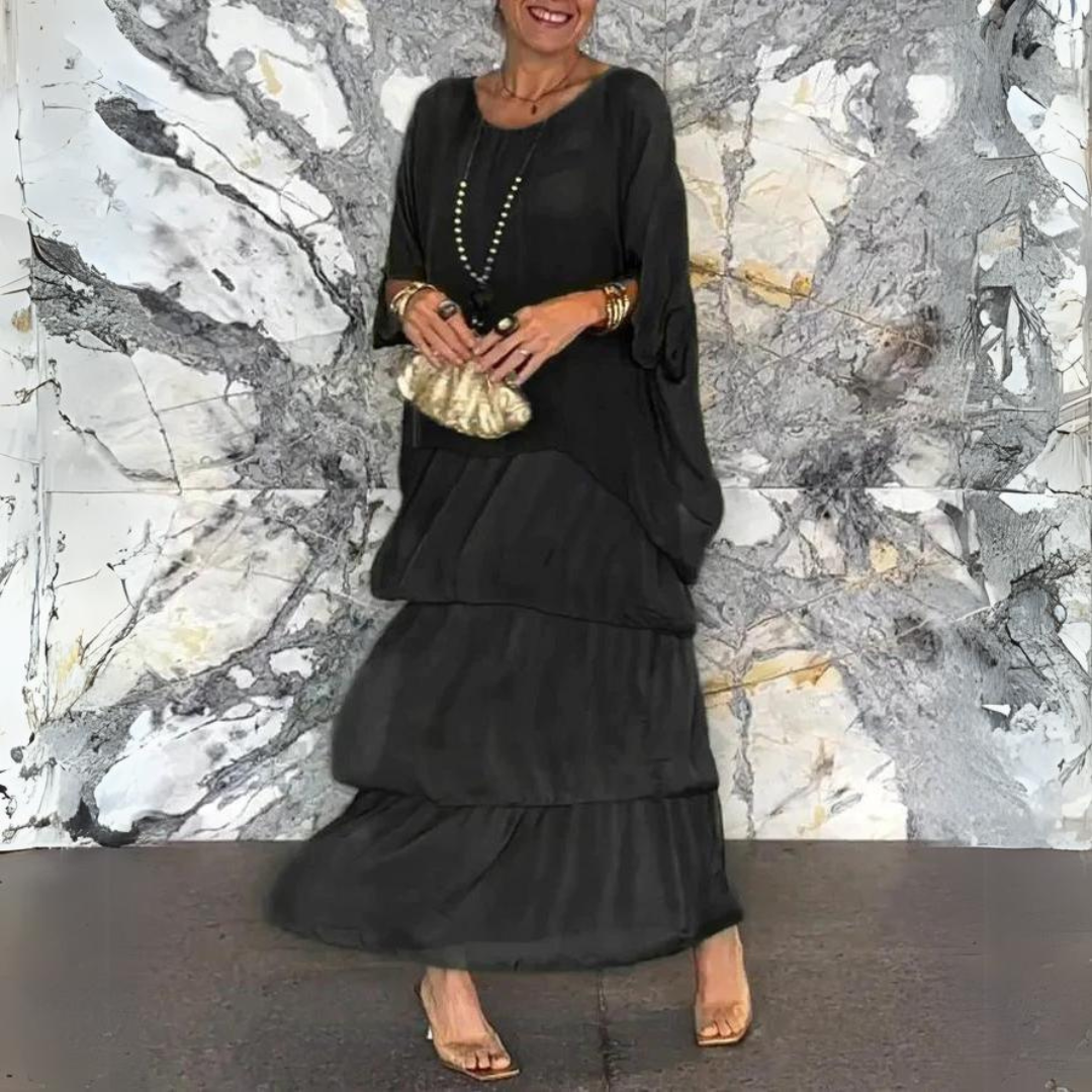 Elegante Frau in schwarzem Maxikleid vor marmorierter Wand, hält goldene Clutch, trägt goldene Accessoires und Sandalen. Fashion, Abendmode, Stil.