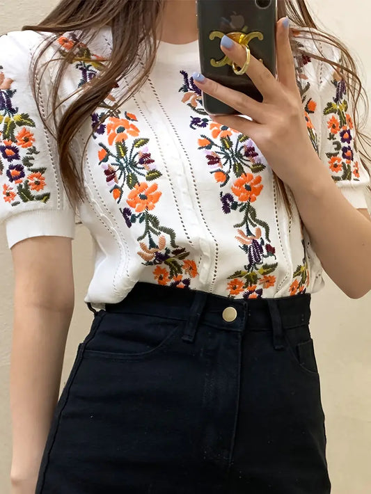 Frau trägt weißes T-Shirt mit buntem Blumenmuster und schwarzer Jeans. Mode, Damenbekleidung, florales Design, trendiger Look.