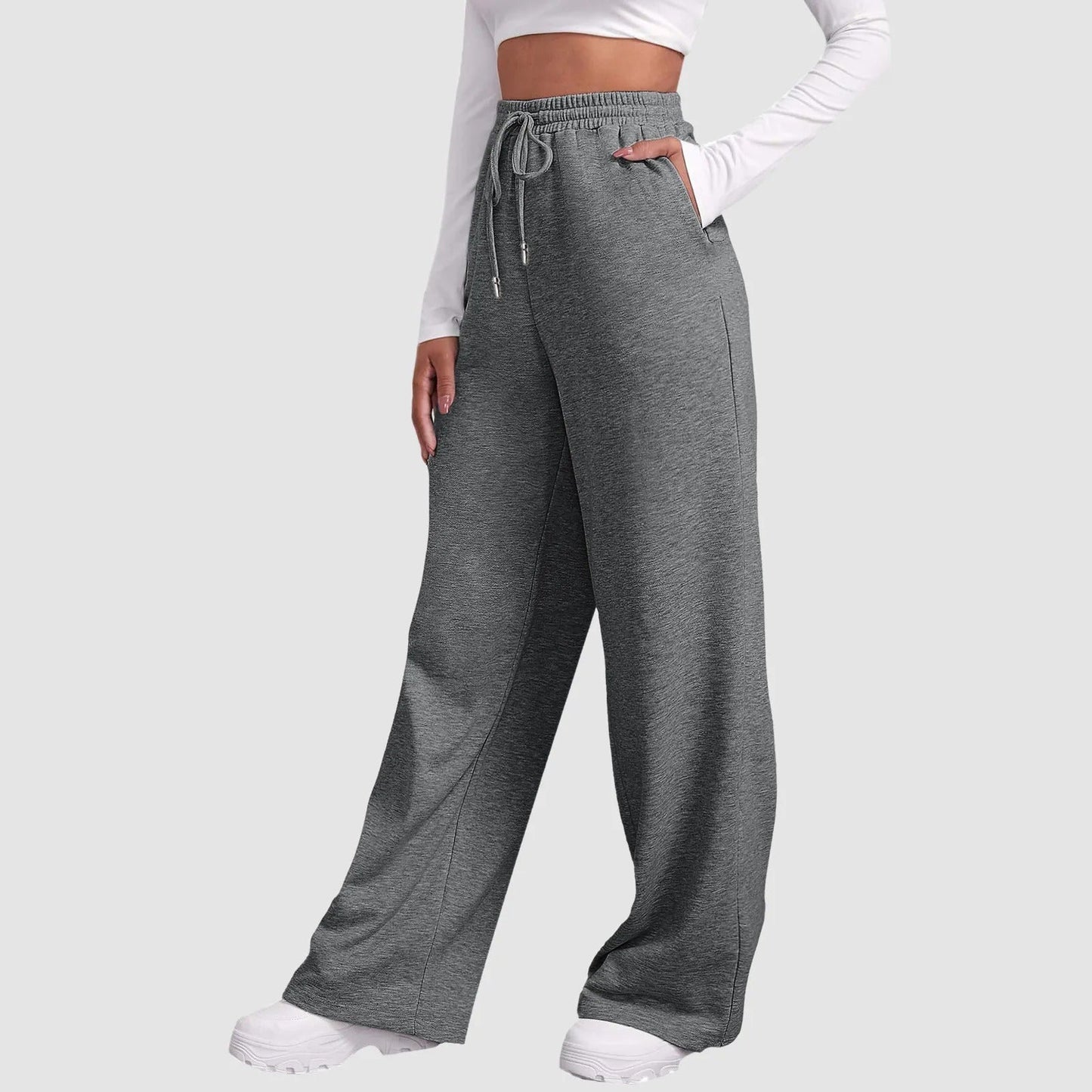 Frau in grauer Jogginghose mit weitem Bein und weißem Langarmshirt, sportlich, bequem, modisch, ideal für Freizeit und Fitness.