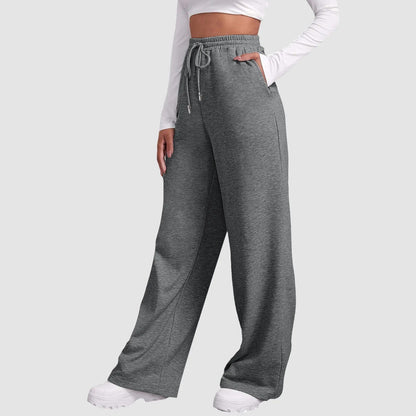 Frau in grauer Jogginghose mit weitem Bein und weißem Langarmshirt, sportlich, bequem, modisch, ideal für Freizeit und Fitness.