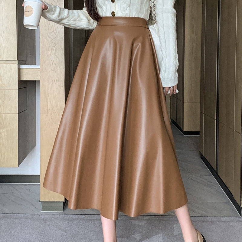 Frau in braunem Lederrock und weißem Strickpullover hält Kaffeebecher. Modetrend, eleganter Herbstlook, stilvolle Damenbekleidung.