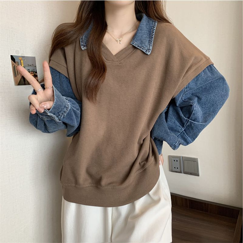 Frau in braunem Pullover mit Jeanshemd-Ärmeln zeigt Peace-Zeichen. Modetrend, lässiger Stil, Damenmode, Herbstoutfit, Streetwear.