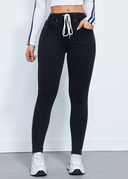 Frau in schwarzer Jogginghose mit Kordelzug, weißem Langarmshirt und weißen Sneakers. Sportliche Damenmode, bequeme Freizeitkleidung.