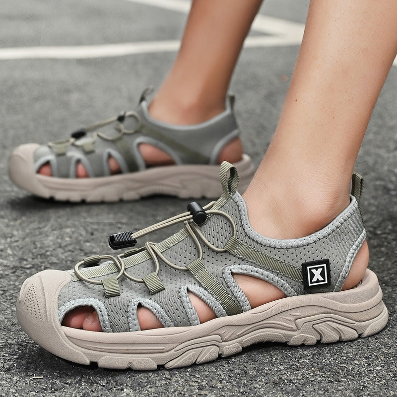 Graue Outdoor-Sandalen mit robusten Sohlen und verstellbaren Schnürsenkeln auf Asphalt. Ideal für Wandern und Freizeitaktivitäten.