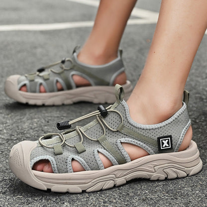 Graue Outdoor-Sandalen mit robusten Sohlen und verstellbaren Schnürsenkeln auf Asphalt. Ideal für Wandern und Freizeitaktivitäten.