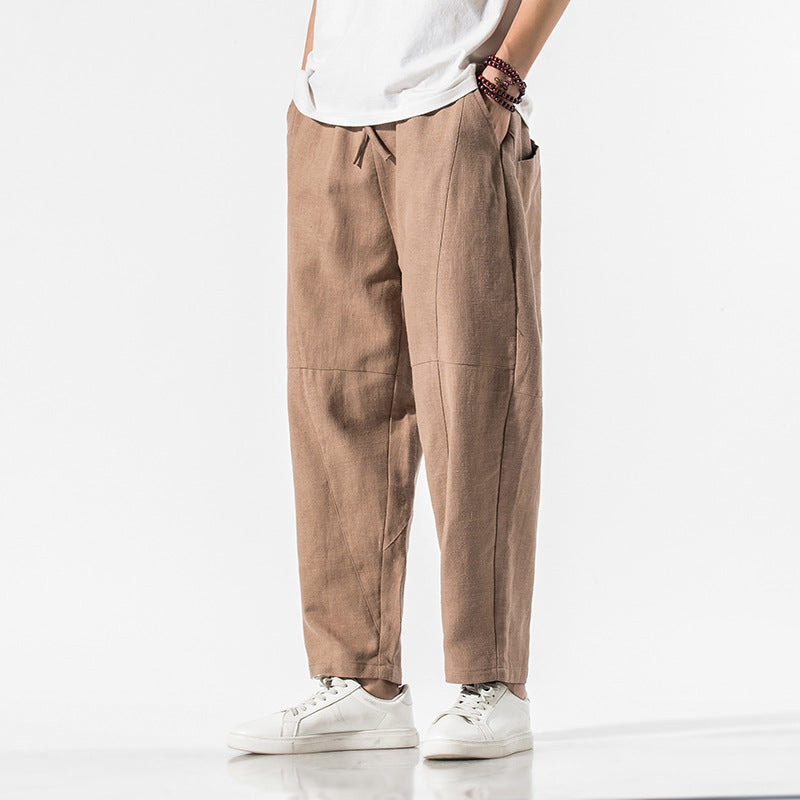 Person trägt beige Leinenhose und weiße Sneakers vor weißem Hintergrund. Modetrend, lässiger Stil, Herrenbekleidung, komfortable Passform.
