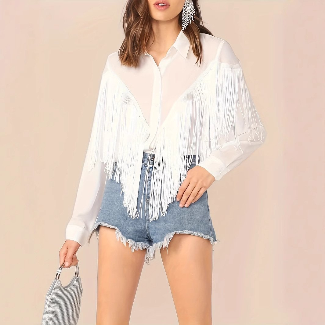 Frau in weißer Fransenbluse und blauen Jeansshorts, hält eine kleine Handtasche. Modetrend, Sommeroutfit, lässiger Stil.