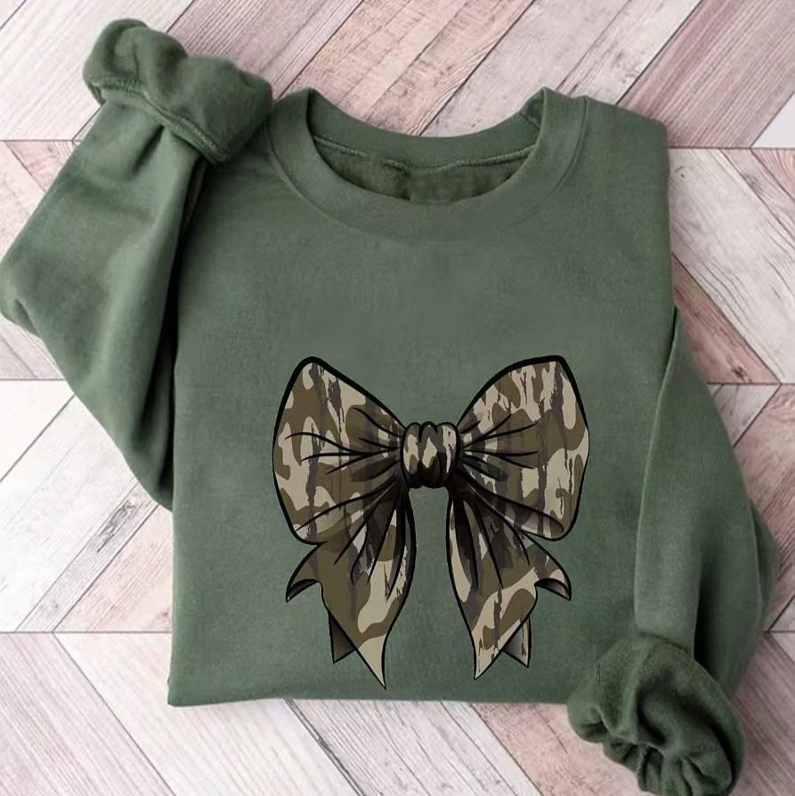 Grünes Sweatshirt mit Camouflage-Schleifenmotiv auf Holzfußboden. Modisches Design, lässiger Stil, ideal für Herbstmode.