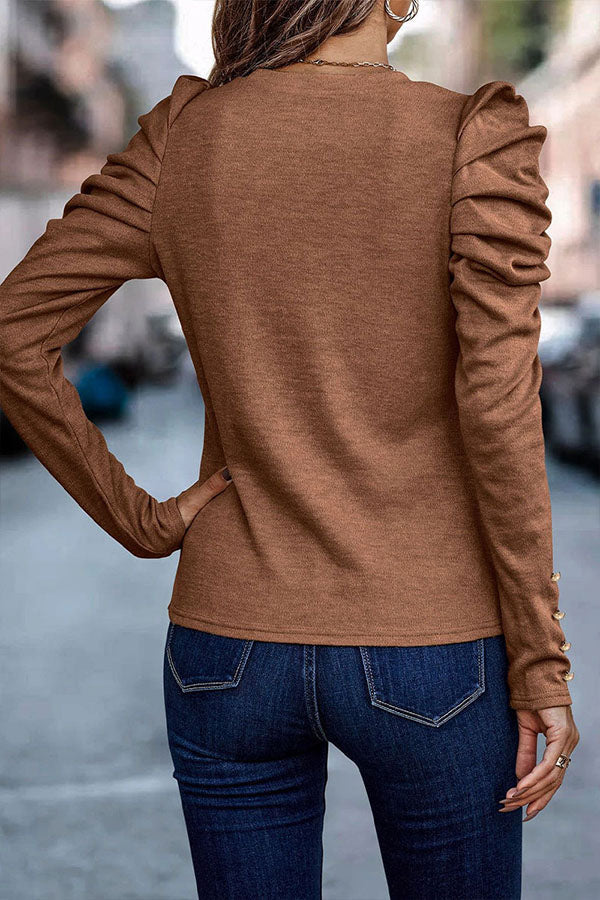Frau in braunem Langarmshirt mit Rüschenärmeln und blauer Jeans, Rückansicht, städtische Straße im Hintergrund. Modetrend Herbstmode Damenbekleidung.