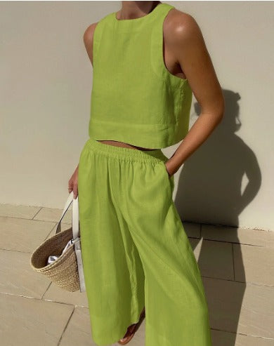 Frau in grünem Leinen-Zweiteiler mit ärmellosem Top und weiter Hose, hält eine Strohtasche. Sommermode, minimalistischer Stil, trendige Kleidung.