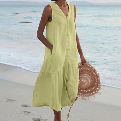 Frau in ärmellosem, hellgrünem Sommerkleid am Strand, hält einen Strohhut. Perfekt für Strandmode, Sommerkleider, Damenmode.