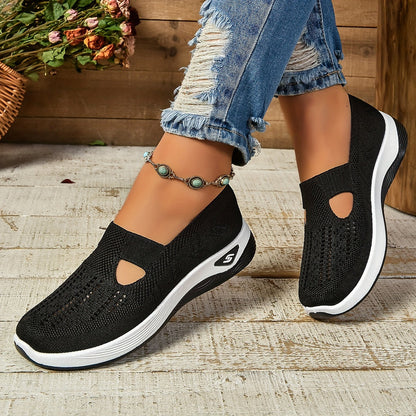 Schwarze Damen-Sneaker mit weißer Sohle, getragen mit zerrissenen Jeans und Fußkettchen, auf Holzboden. Bequeme, modische Freizeitschuhe.