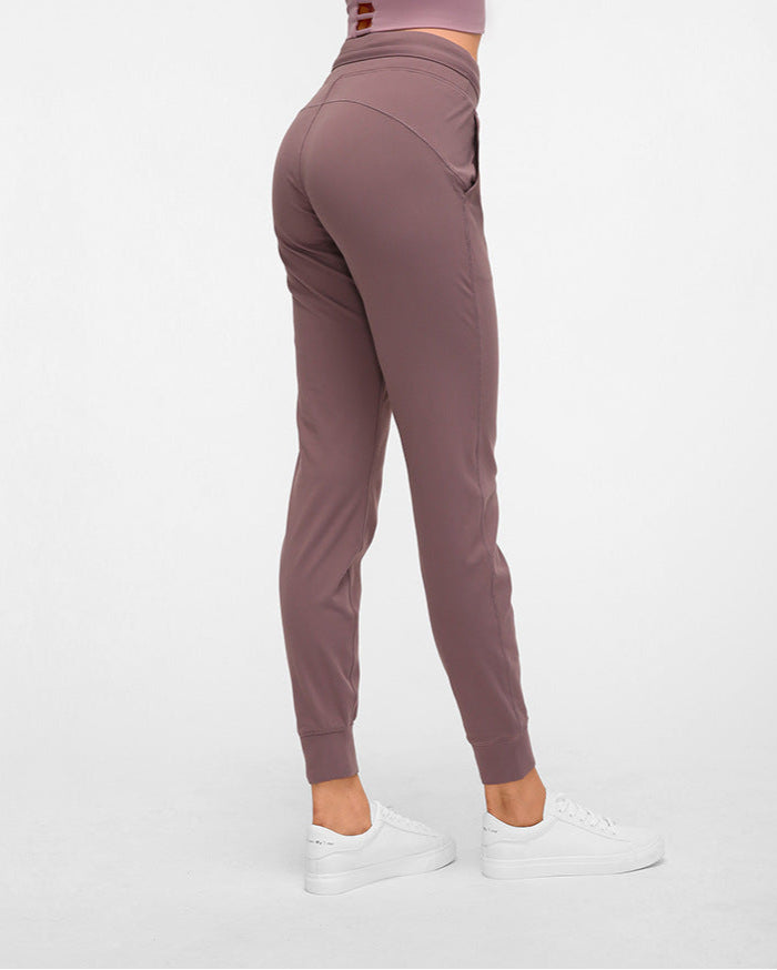 Frau in lila Jogginghose und weißen Sneakers, seitlich stehend. Sportbekleidung, Fitnessmode, bequeme Damenhose, Freizeitlook.