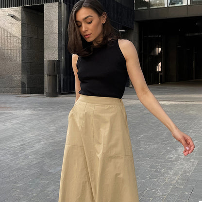 Frau in schwarzem ärmellosen Top und beiger Hose steht auf modernem Stadtplatz. Modetrend, urbane Kleidung, stilvolle Frau, Sommeroutfit.