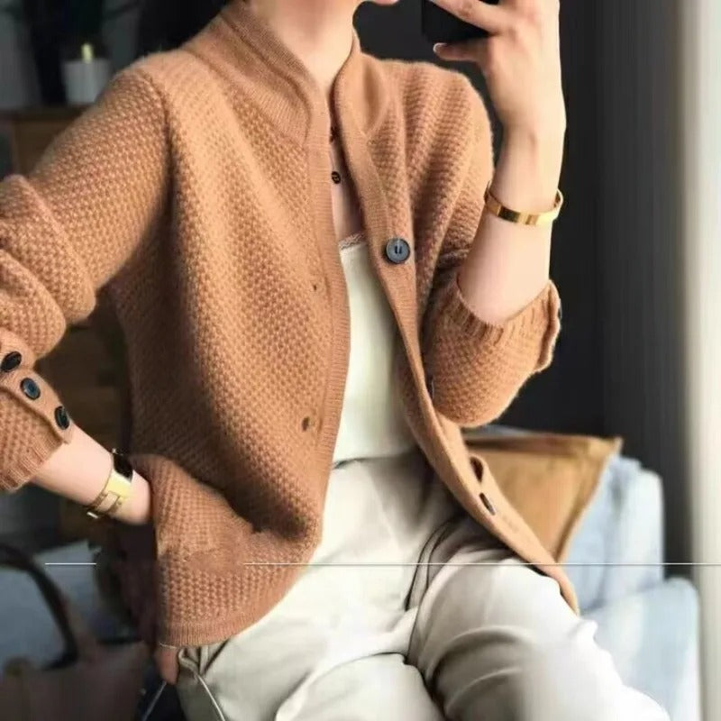Frau in beiger Strickjacke mit Knöpfen, weißem Top und beiger Hose, hält Smartphone. Modetrend, Herbstmode, Damenbekleidung, eleganter Look.