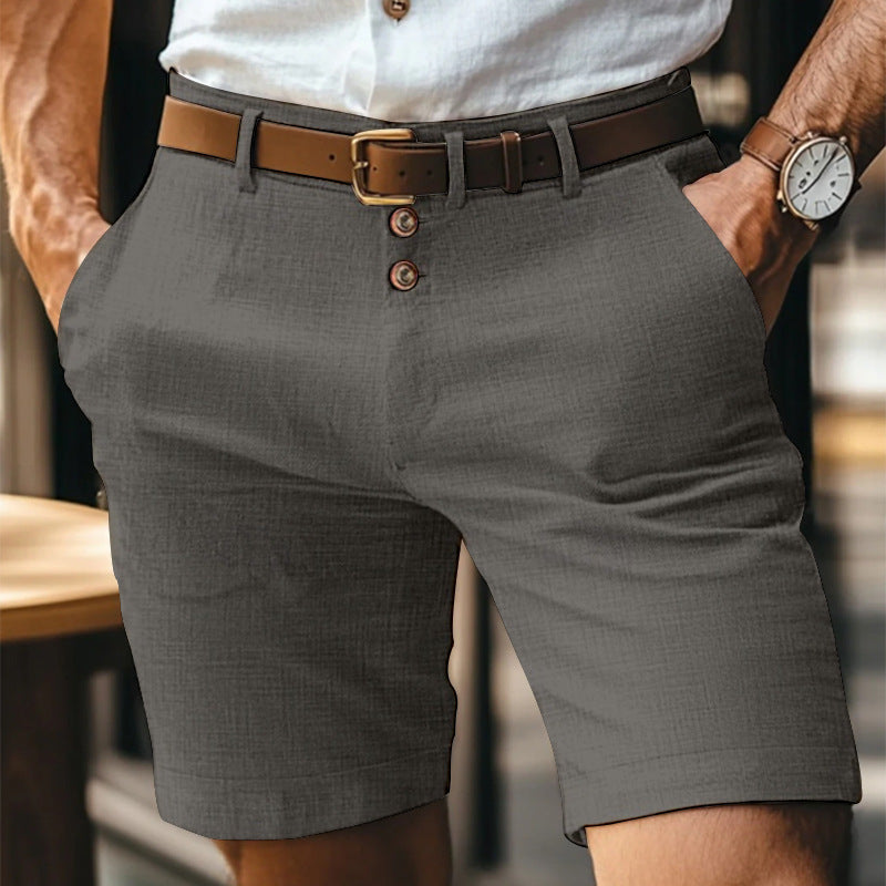 Mann in grauen Shorts mit braunem Ledergürtel und weißem Hemd, trägt eine Armbanduhr. Elegante Sommermode für Herren.