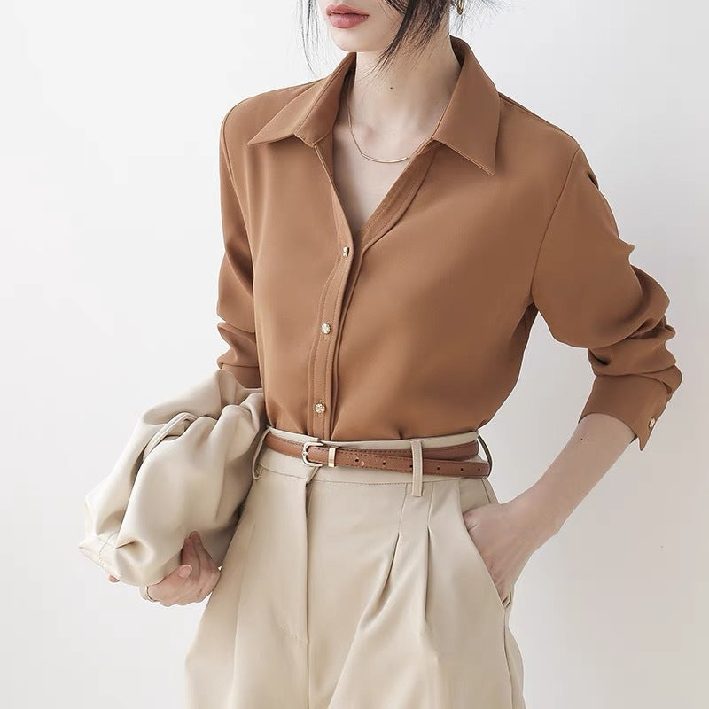 Frau in brauner Bluse und beigen Hosen, hält beigen Mantel. Elegante Mode, minimalistischer Stil, Business-Look, Damenbekleidung.