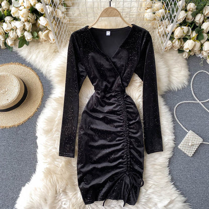 Schwarzes, glitzerndes Wickelkleid mit Raffung, umgeben von weißen Rosen, Strohhut und Perlenhandtasche auf flauschigem Teppich. Elegantes Abendoutfit.