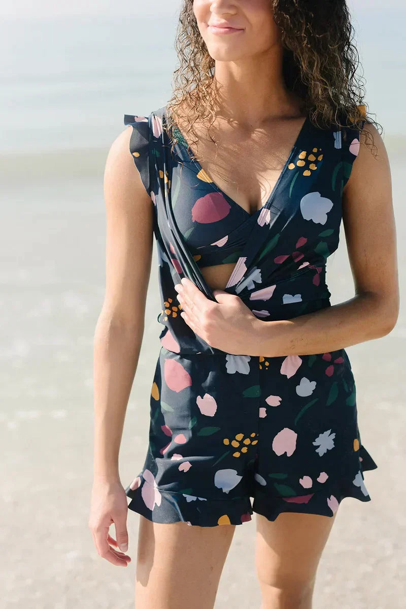 Frau am Strand in geblümtem Sommerkleid, lächelnd, mit lockigem Haar. Perfektes Outfit für Strandmode und Sommerkleidung.
