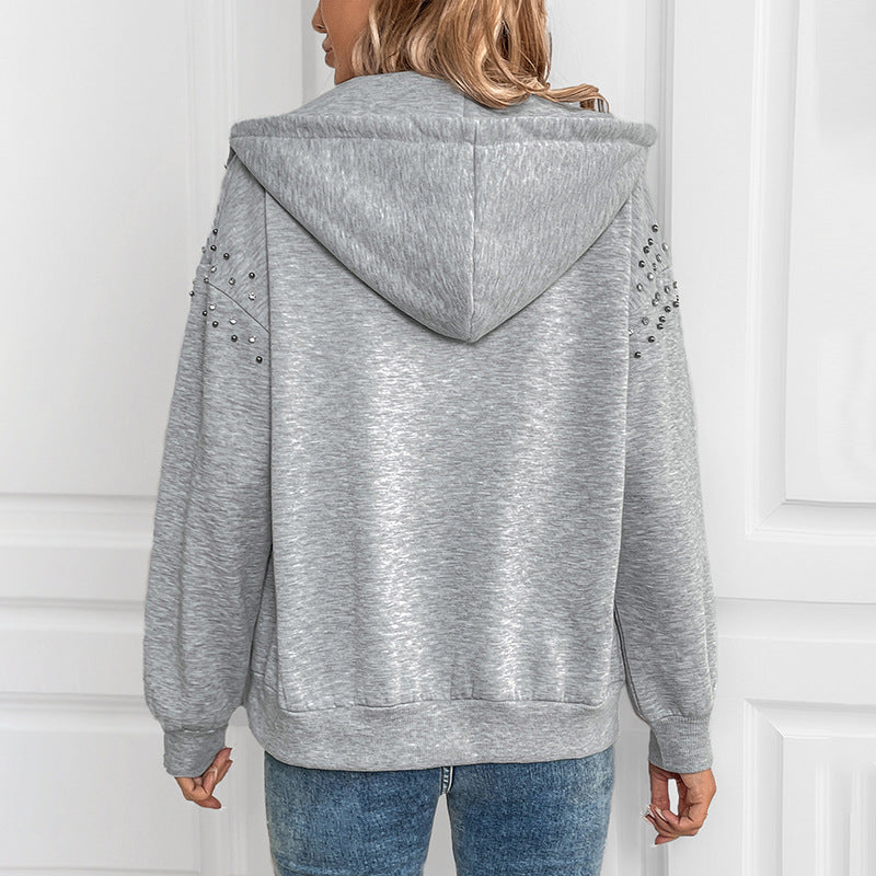 Frau in grauem Kapuzenpullover mit Nieten-Details, Rückansicht. Modischer Hoodie, lässiger Stil, ideal für Herbstmode.