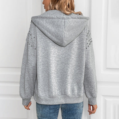 Frau in grauem Kapuzenpullover mit Nieten-Details, Rückansicht. Modischer Hoodie, lässiger Stil, ideal für Herbstmode.