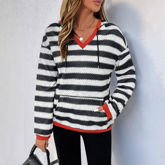 Frau in gestreiftem Pullover mit Kapuze, schwarz-weiß mit roten Akzenten, hält schwarze Handtasche. Modetrend, lässiger Stil, Herbstmode.
