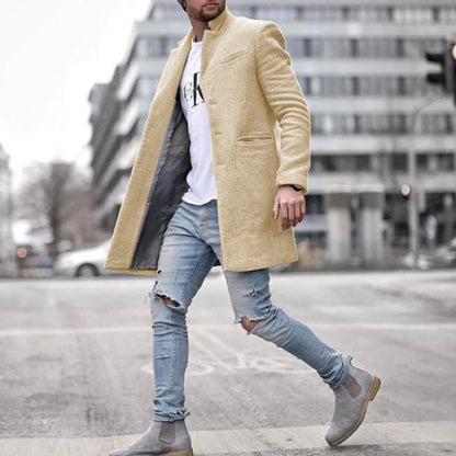 Mann in beigem Mantel, zerrissene Jeans und graue Stiefel überquert Straße in urbaner Umgebung. Modetrend, Herrenmode, Streetstyle.
